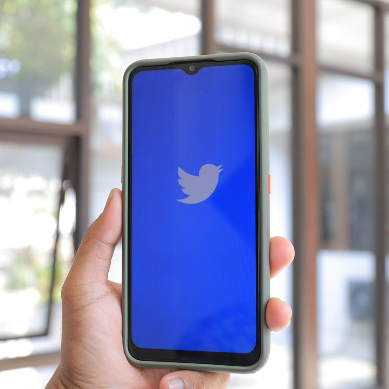 Hand holding a smartphone showing the X (Twitter) logo, a creator preparing an X growth strategy in 2026